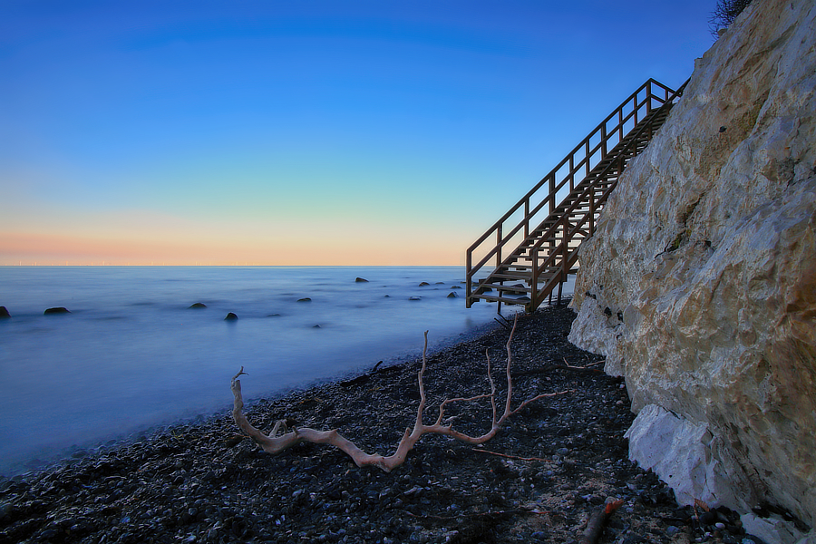 Langzeitbelichtung an einer Steilküste mit Treppe zum Meer in der blauen Stunde.