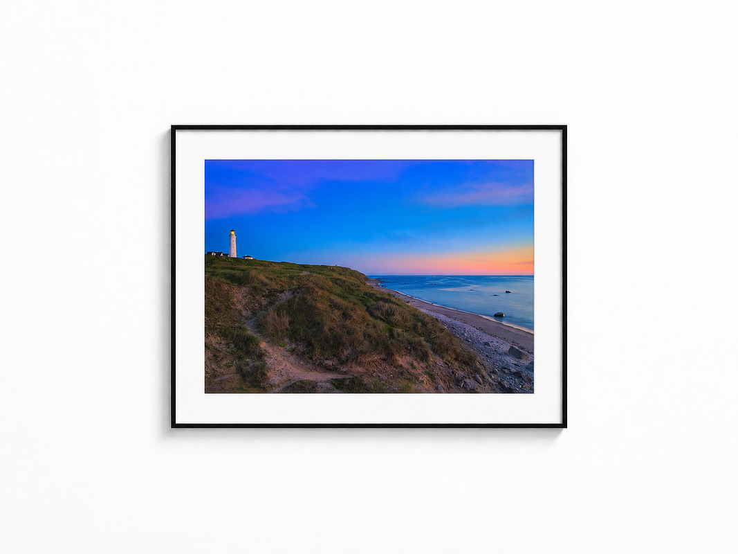 Visualisierung der Fotografie „Horizontwächter“ in schwarzem Rahmen mit weißem Passepartout an einer hellen Wand. Leuchtturm auf einer grasbewachsenen Steilküste über dem ruhigen Meer bei blau-rosa Abendhimmel.