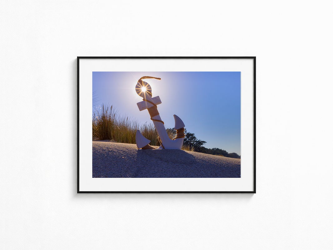 Visualisierung der Fotografie „Lichtanker“ in schwarzem Rahmen mit weißem Passepartout an einer hellen Wand. Anker vor dunklem Holz mit kleinen warmen Lichtern, kühlem Blau und warmem Horizontleuchten; im Herzen des Ankers fängt sich das Licht.