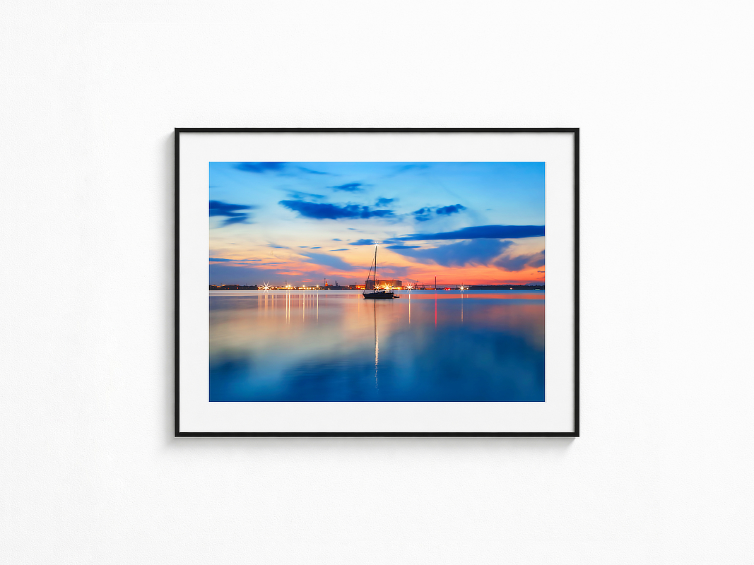 Visualisierung der Fotografie „Spiegelmeer“ in schwarzem Rahmen mit weißem Passepartout an einer hellen Wand. Ruhiges Meer unter weitem Abendhimmel mit intensiver Spiegelung des Lichts und der Farben auf der nahezu glatten Wasseroberfläche.